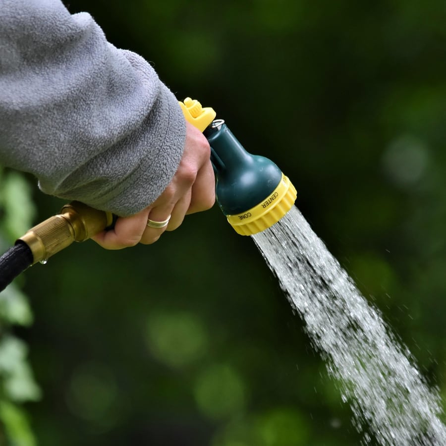 Landschaftsgärtner bewässert mit der Gartenbrause eine frisch angelegte Grünfläche