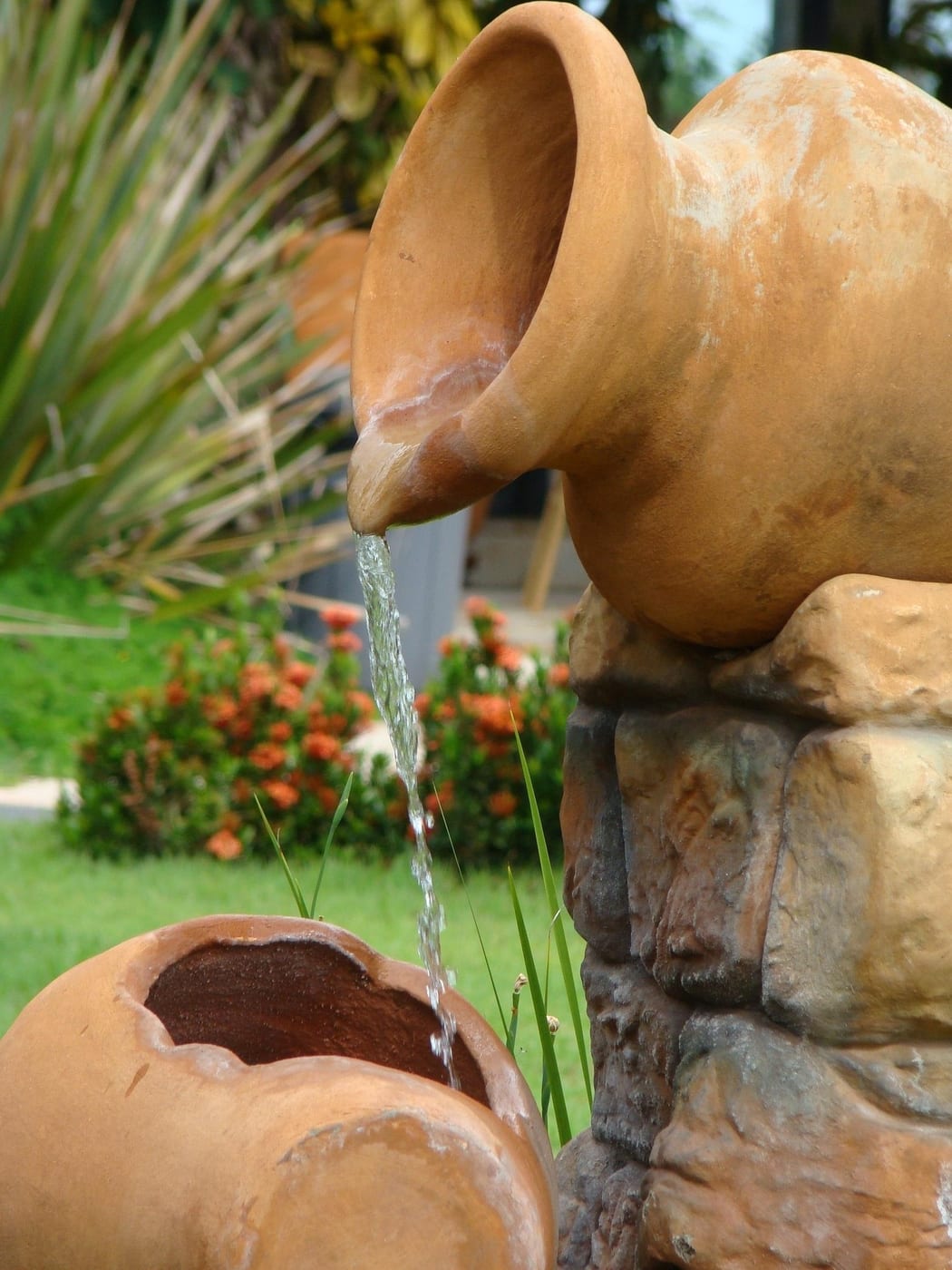 Vom Landschaftsgärtner angelegtes Wasserspiel aus einem Tonkrug in einem dicht bepflanzten Gartenbereich